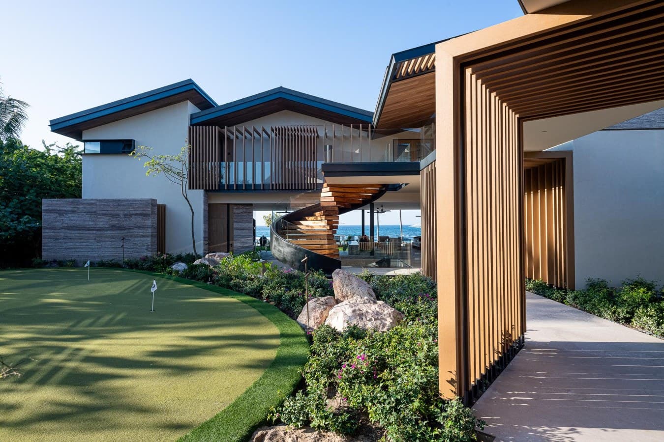 A stunning beachfront property with striking architectural design features modern wood slat detailing, multiple entertaining levels, and manicured landscaping, including a private putting green for golf enthusiasts.