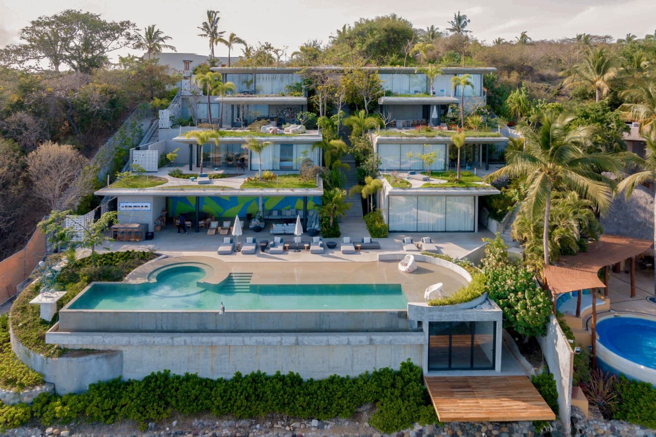 This stunning hillside property showcases modern tiered architecture with lush tropical gardens, a pristine infinity pool, and breathtaking natural surroundings—a truly remarkable vacation retreat.