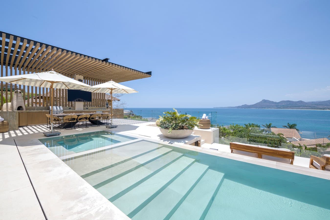 Stunning coastal property with pristine pool and mountains framing the horizon. The modern pergola and elegant lounge area create your perfect oceanfront sanctuary.