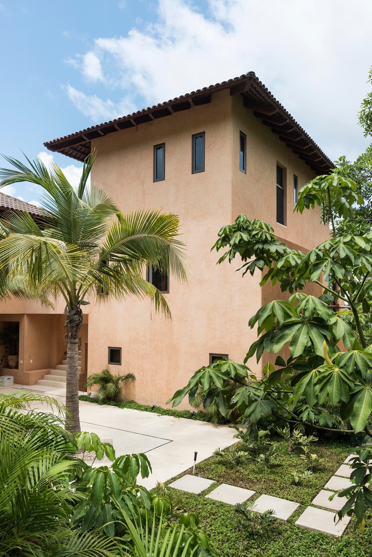 A striking terracotta villa nestled in lush tropical gardens, featuring Spanish-style architecture with a traditional tile roof and surrounded by swaying palms.