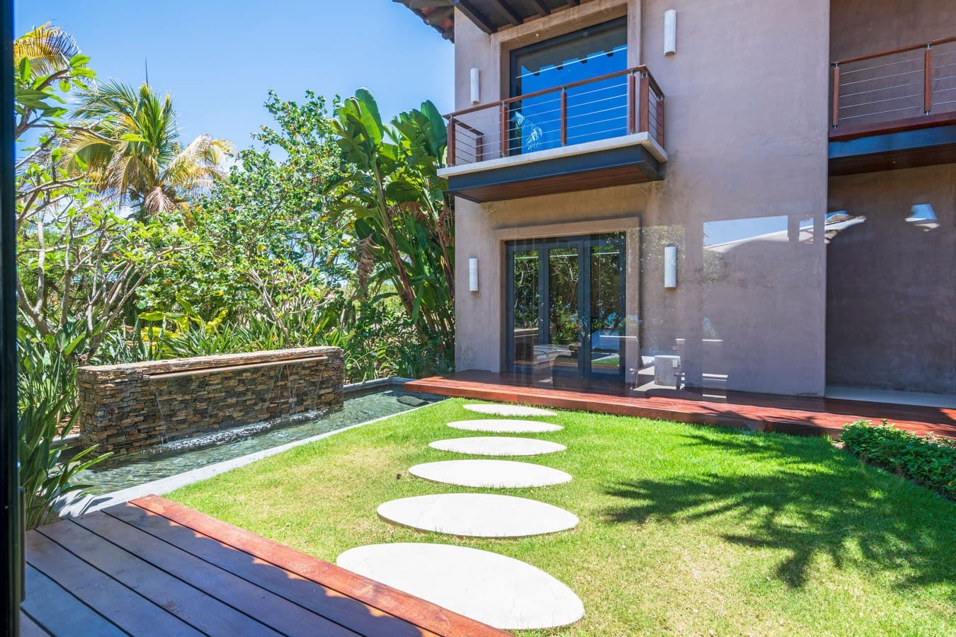 Modern tropical retreat featuring stepping stones across lush green lawn, surrounded by palm trees and tropical foliage, with elegant balconies overlooking your private outdoor sanctuary.