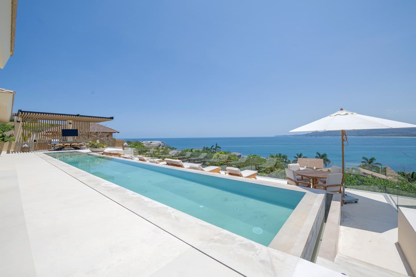 An aerial or elevated view of a coastal vacation rental property featuring a sparkling pool and outdoor lounging area overlooking the ocean.