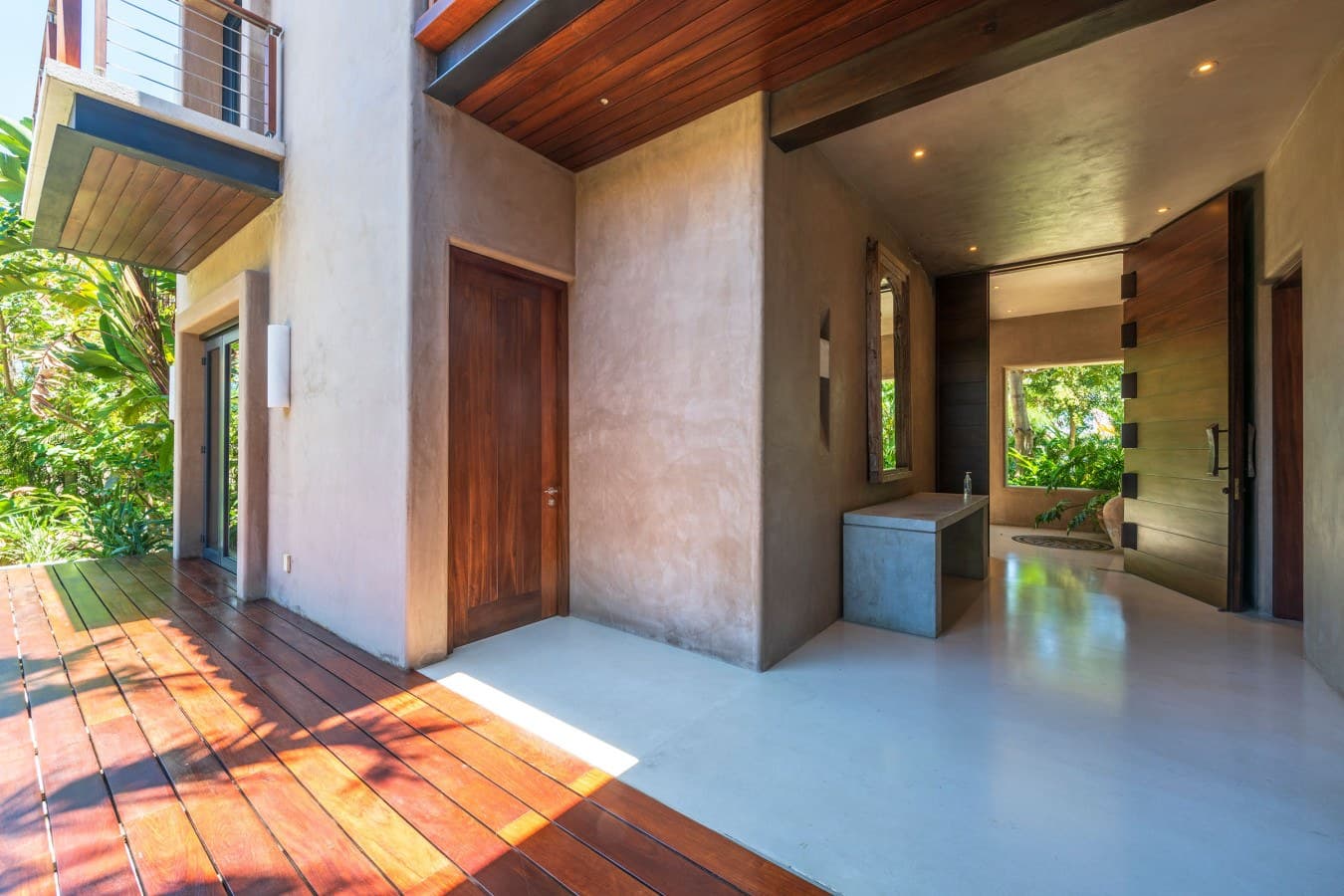 Modern tropical design blends seamlessly with natural surroundings. Warm wood accents and polished concrete create an inviting open-air entrance with lush greenery framing your arrival.