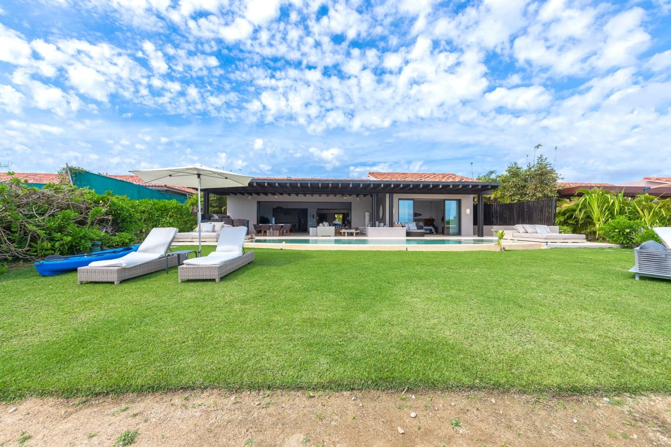 Your private paradise with sweeping lawn, inviting pool, and spacious covered terrace. Lush gardens frame this tranquil outdoor retreat under a brilliant sky.