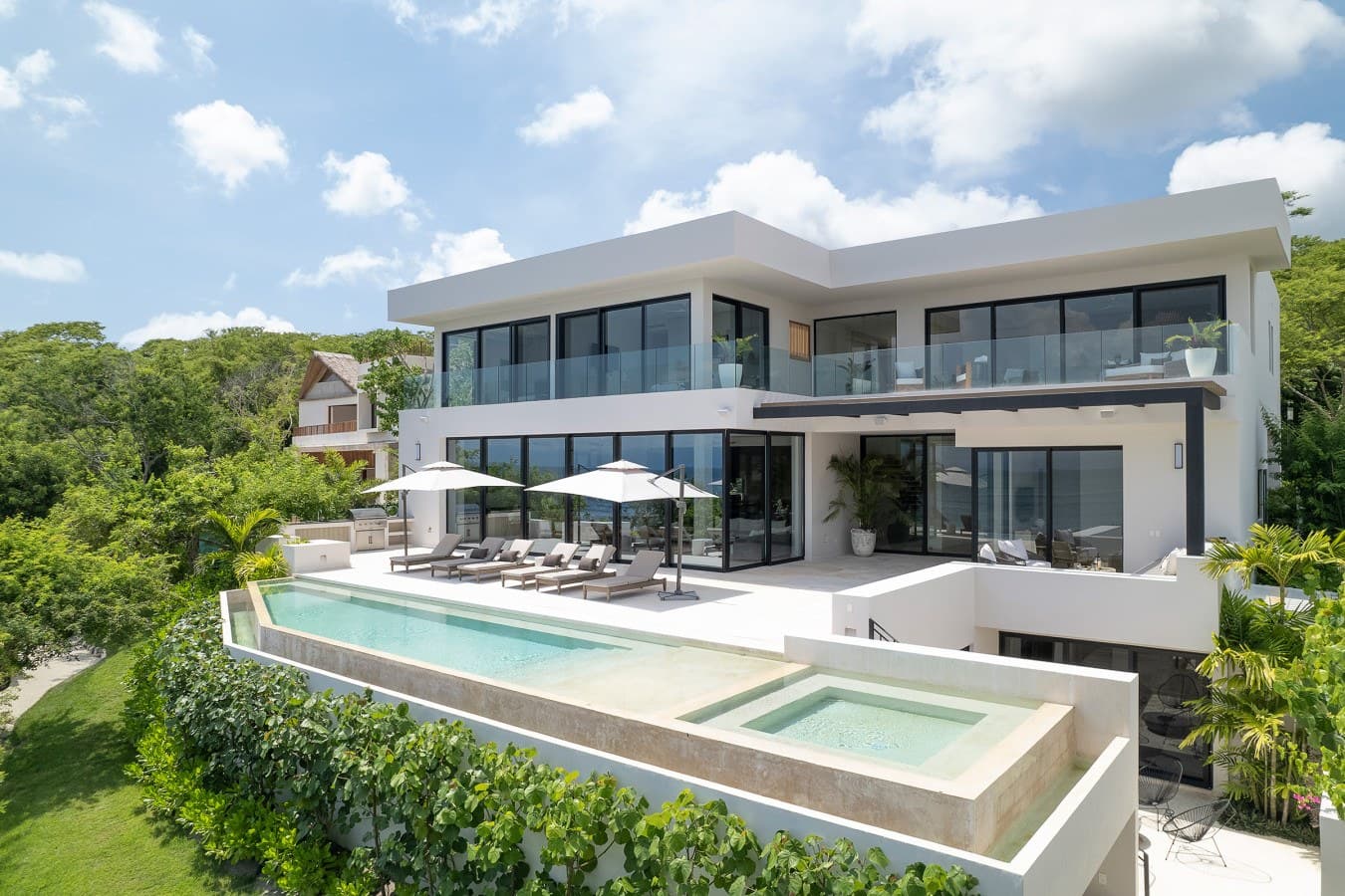 A stunning modern villa perched among lush tropical greenery, featuring expansive terraces, a pristine pool, and sleek contemporary architecture—your luxurious private retreat awaits.