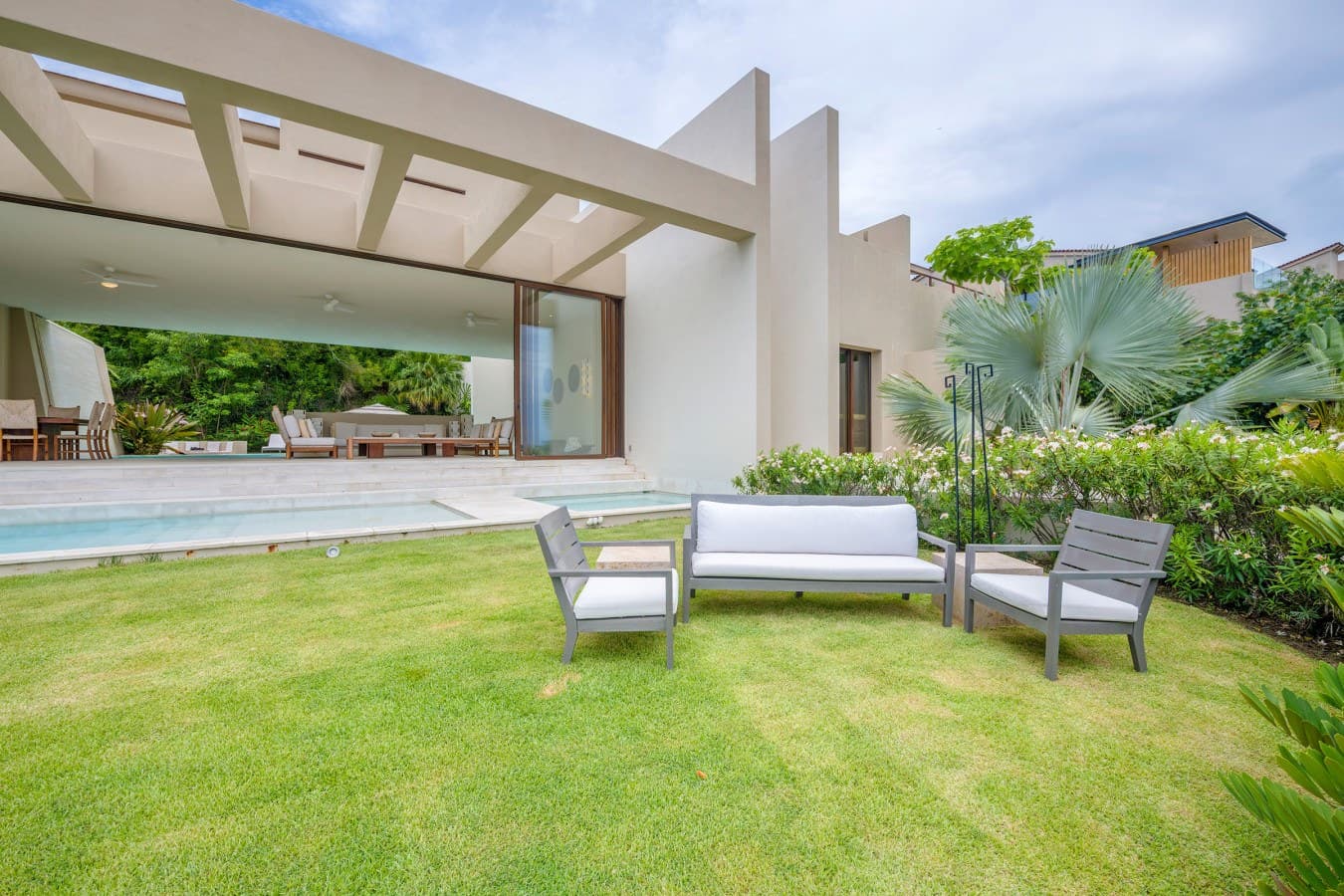 Modern villa exterior with private pool, manicured garden, and covered terrace offering stylish outdoor living space surrounded by lush tropical greenery.