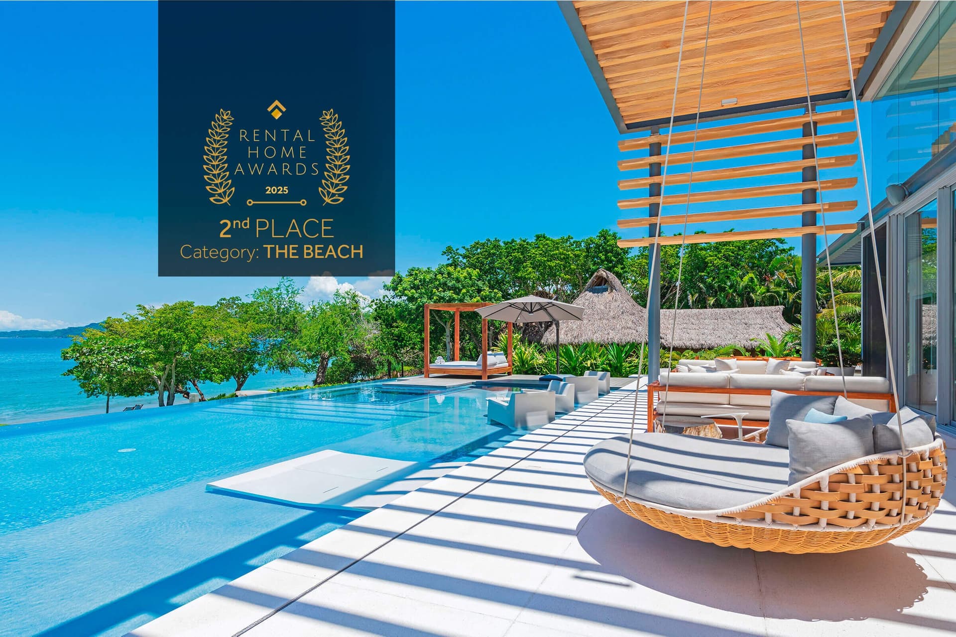 A pristine infinity pool flows seamlessly toward turquoise waters and lush tropical gardens, with modern lounging spaces under a striking wooden pergola—your private paradise awaits.