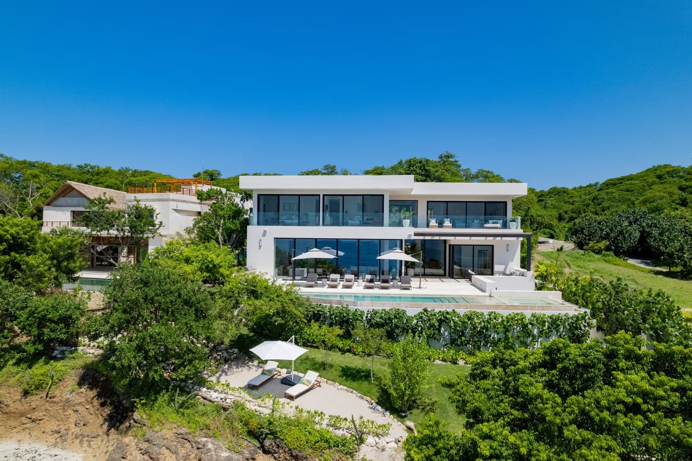 A stunning modern villa nestled into lush tropical hillside, featuring a private pool and spacious terraces surrounded by vibrant greenery and ocean breezes.