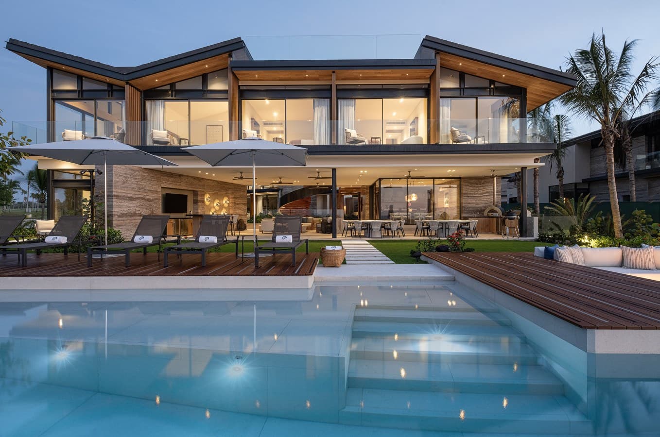 A stunning modern villa surrounded by tropical palms, featuring expansive glass walls and a sparkling pool that seamlessly blends indoor-outdoor living in this luxurious coastal retreat.