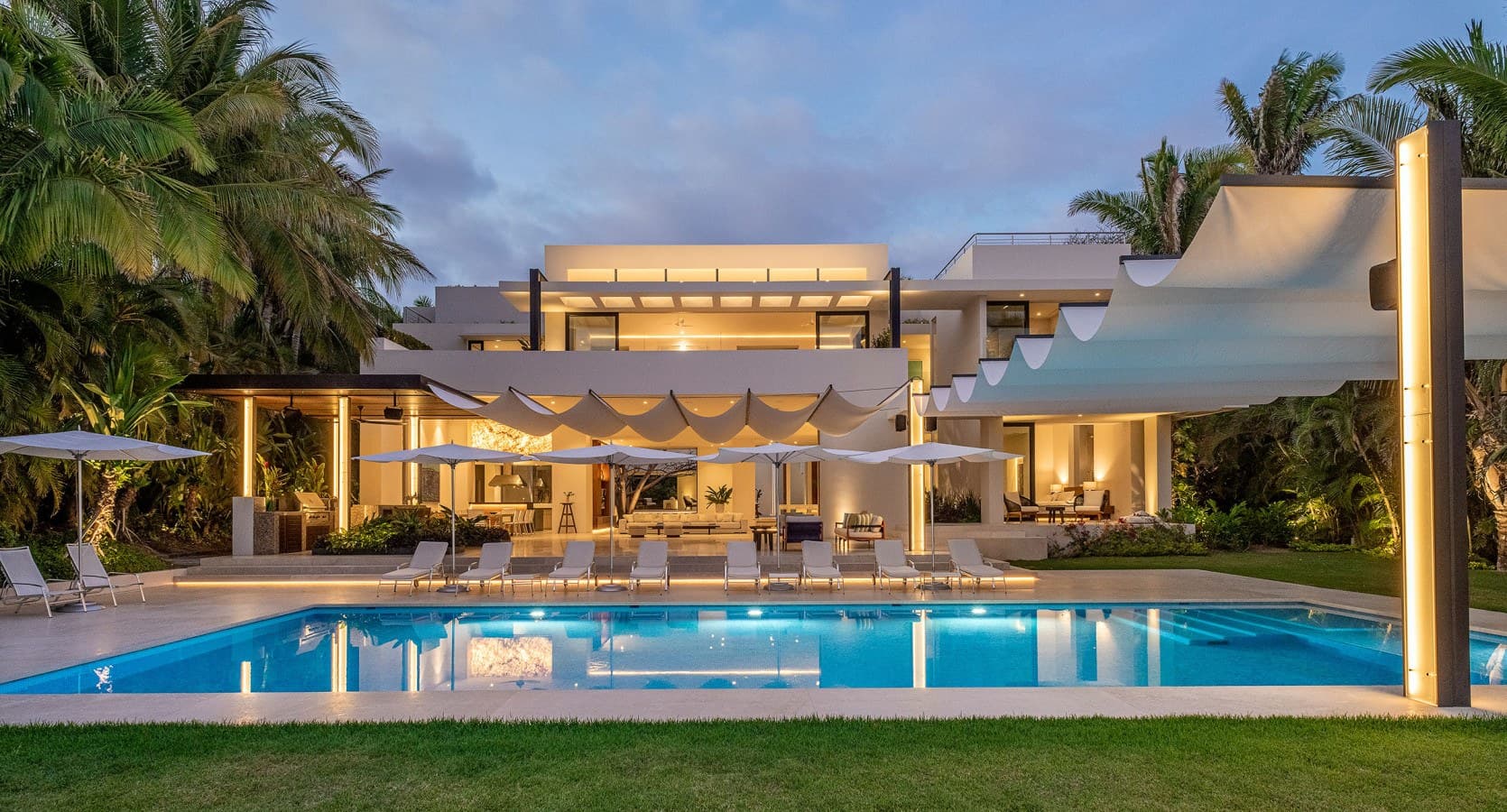 This stunning contemporary villa awaits at twilight, where modern luxury meets tropical paradise. Picture yourself relaxing by the pristine pool, surrounded by swaying palms and warm evening light.