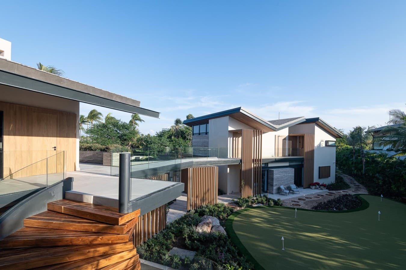 The property features contemporary architecture with natural wood accents, framed by lush tropical palms and landscaped grounds. The modern design blends seamlessly with the surrounding greenery.