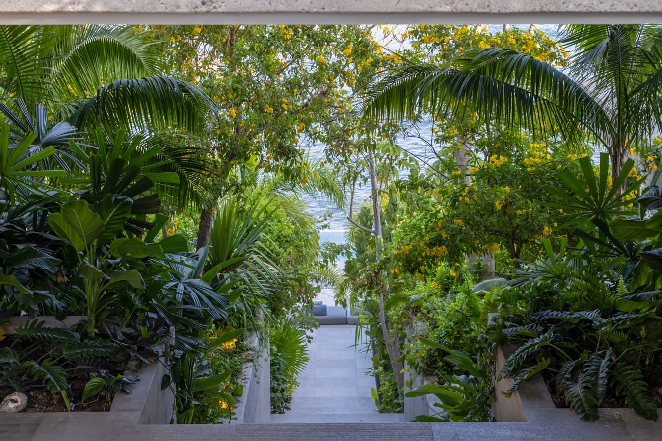 A lush garden pathway leads toward the beach, framed by swaying palms and flowering tropical trees. Feel the ocean breeze as you stroll through this vibrant oasis.