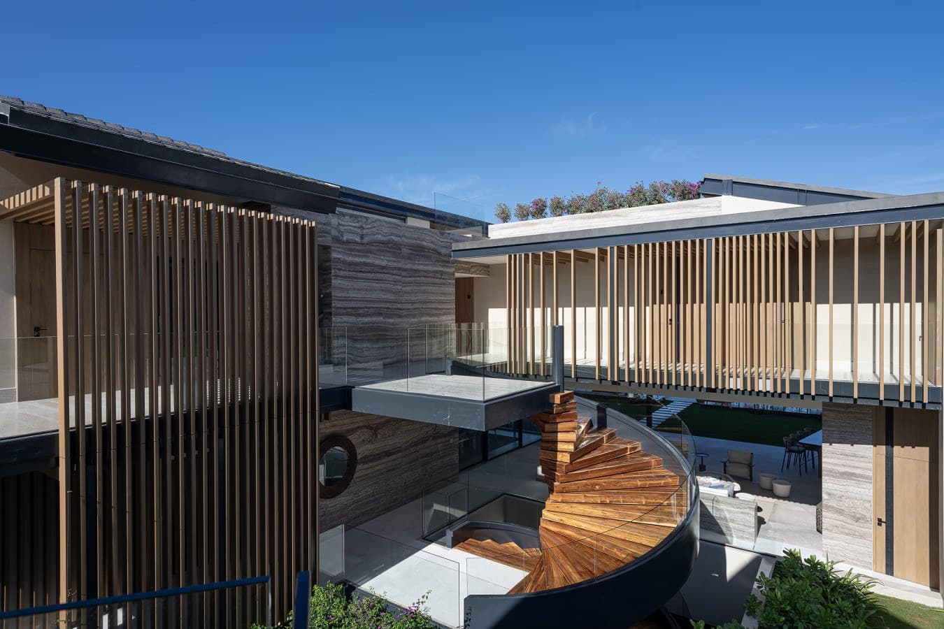 A stunning architectural property featuring modern design with striking wooden slat screens, an inviting spiral staircase, and an elegant courtyard bathed in sunlight.
