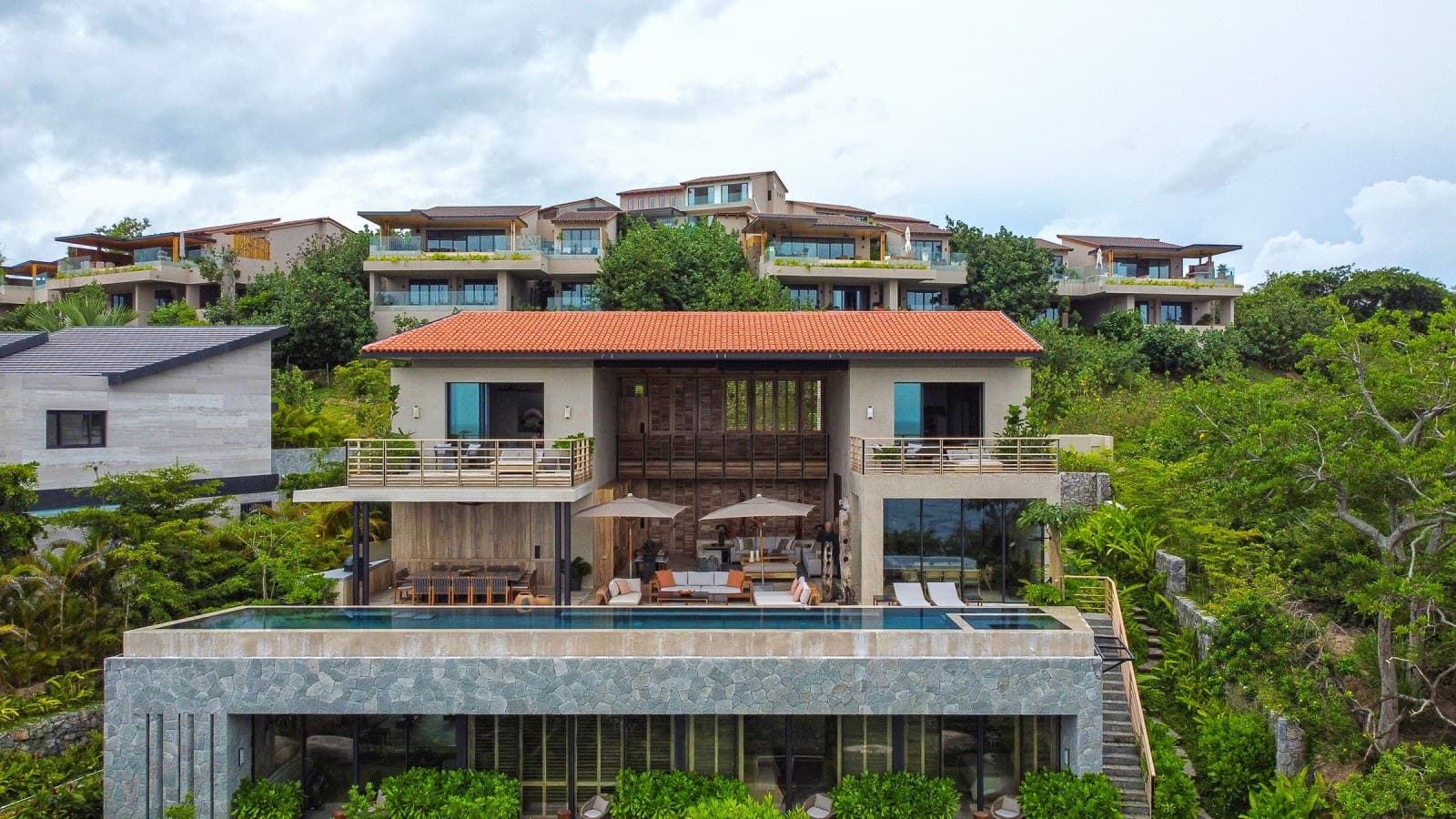 A stunning hillside vacation rental property nestled among lush tropical vegetation, offering modern architectural design with warm terracotta roof accents and expansive terraces for your ultimate relaxation.
