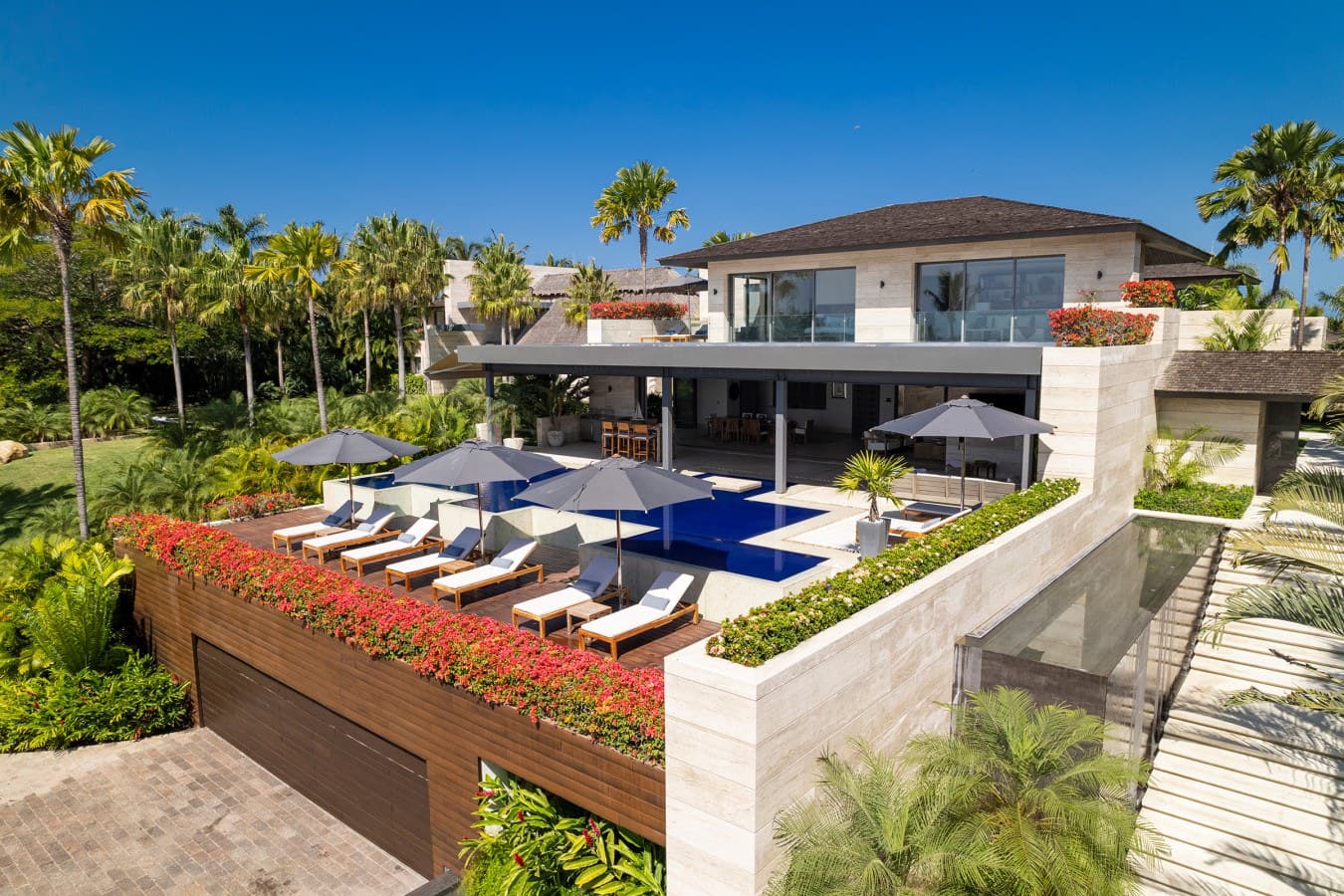A striking modern villa set within lush tropical gardens, featuring a private rooftop terrace complete with pool, sun loungers, and vibrant landscaping—an idyllic retreat beneath swaying palms.