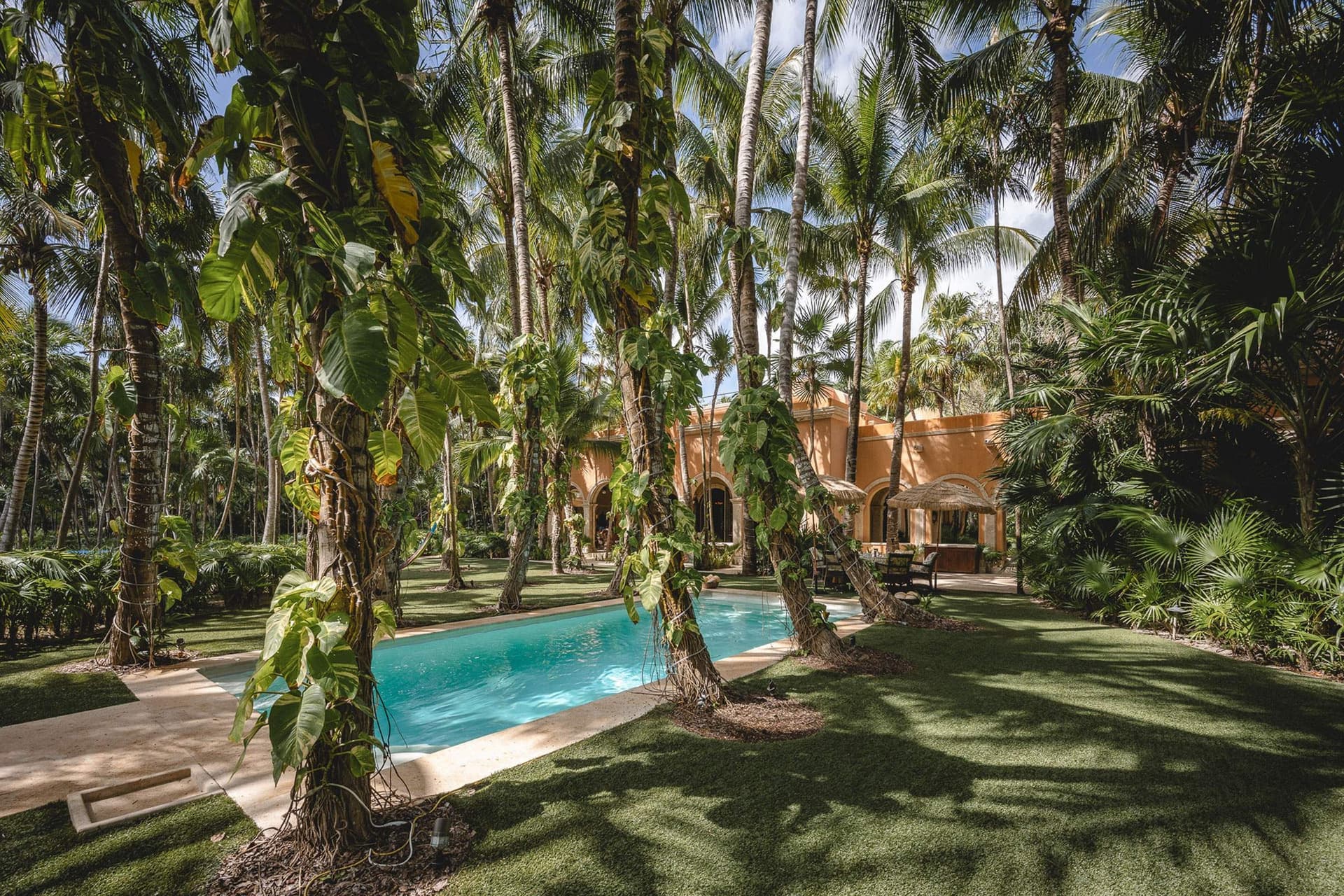 A tropical paradise where towering palms frame the pool area, offering a peaceful oasis surrounded by lush greenery and warm sunshine.