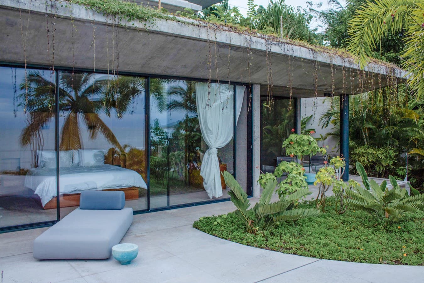 Modern tropical retreat where your sleeping sanctuary opens seamlessly to lush gardens and a relaxing terrace beneath a green roof, blending contemporary design with natural beauty.