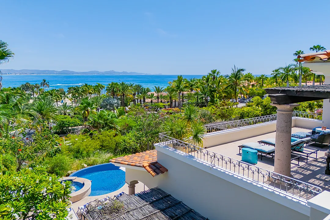Elevated property showcasing a private pool, lush tropical gardens, and expansive ocean views stretching to distant mountains. A serene coastal setting surrounded by palm trees.