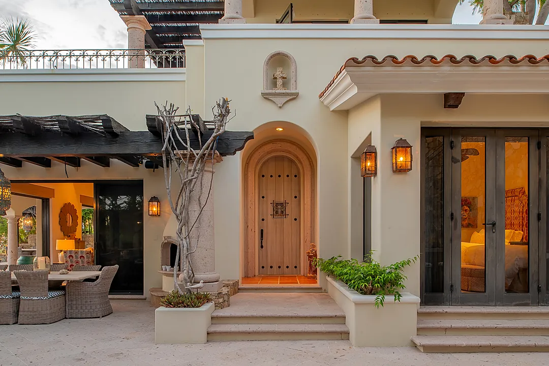 A hacienda-style entrance with arched wooden doors and warm lanterns welcomes you to this elegant coastal retreat, where indoor-outdoor living spaces blend seamlessly into your private patio sanctuary.