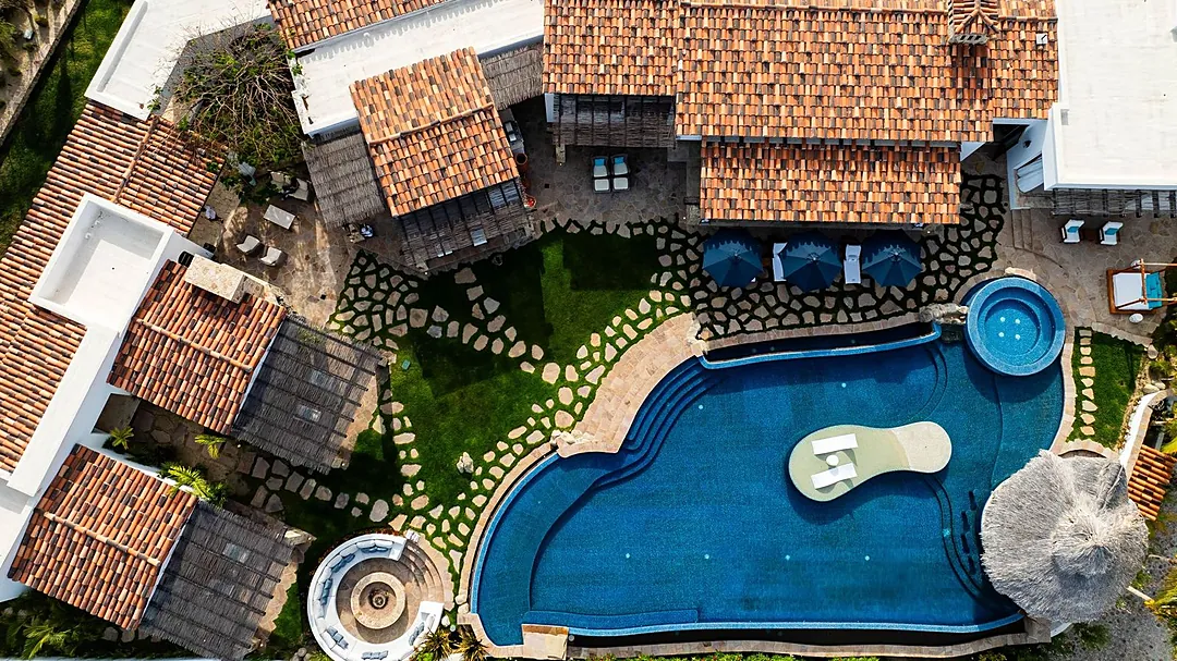 Aerial view showcasing the property's expansive pool area with integrated hot tubs, sunbeds, and multi-level terracotta-roofed buildings set within beautifully landscaped grounds.