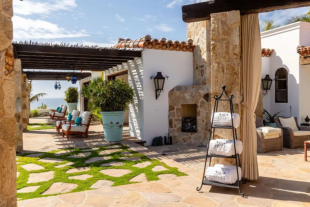 A luxurious outdoor oasis featuring stone accents, outdoor fireplace, and covered seating areas. The property showcases beautiful terracotta tile roofing and Mediterranean-inspired architecture with ocean views.