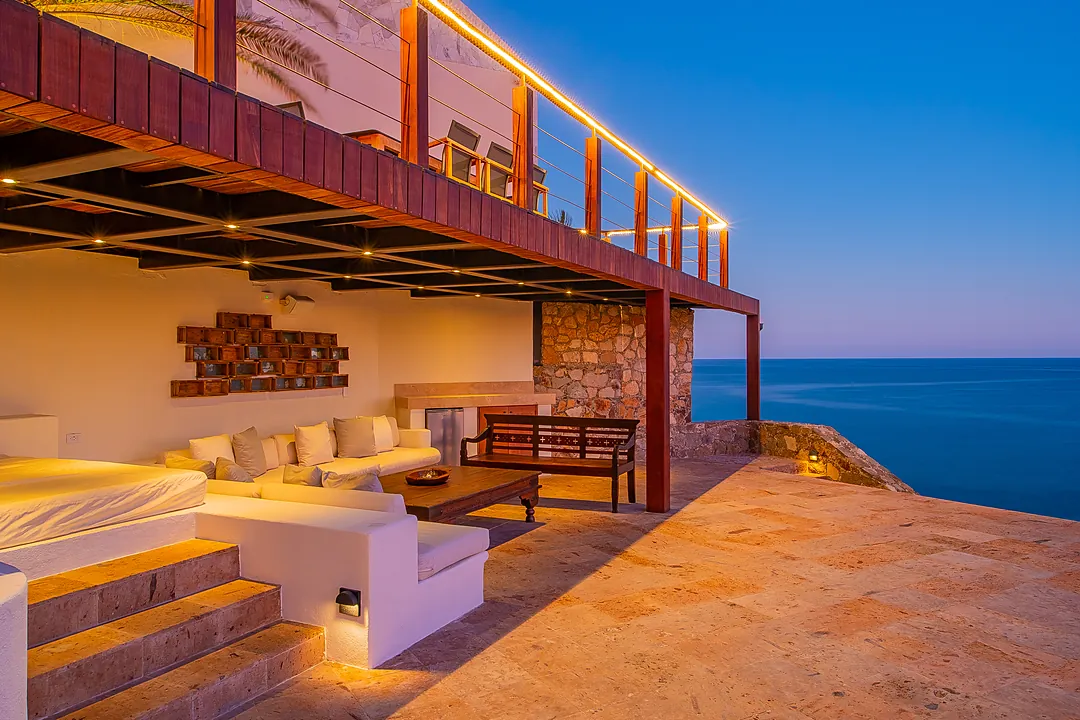 Stunning oceanfront villa showcasing multi-level architecture, elegant stone and wood design, ambient lighting at dusk, and an expansive terrace with breathtaking sea views stretching to the horizon.