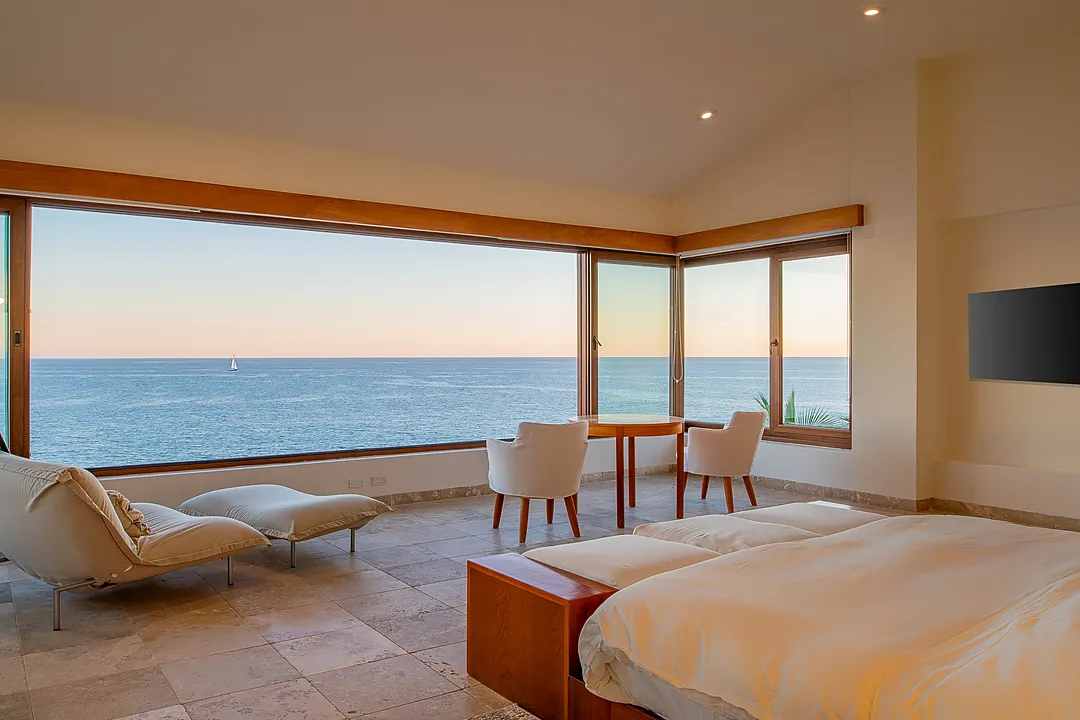 Bedroom 1 (Master) · Drift off to sleep as the gentle sound of waves fills your spacious bedroom, where floor-to-ceiling windows frame endless ocean views and a cozy seating area invites quiet moments.