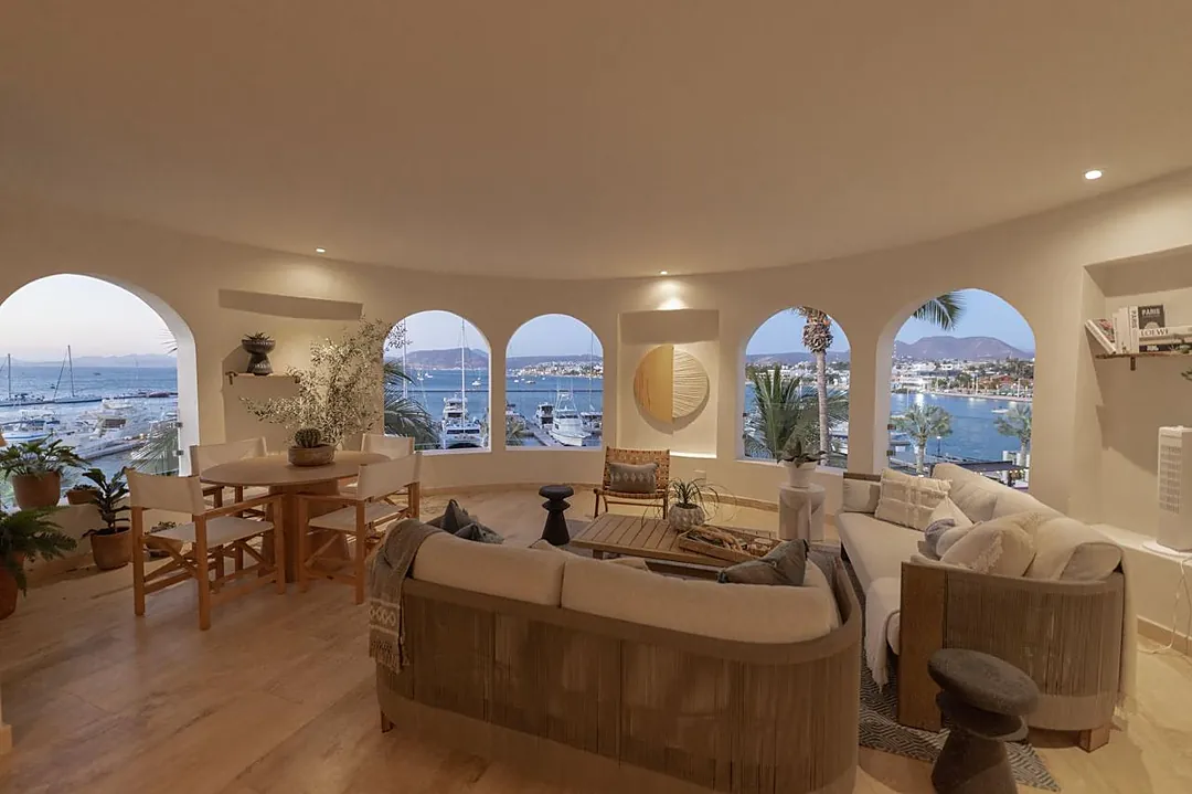 Stunning coastal views frame this elegant living space, where arched windows showcase the marina and surrounding hillsides. Picture yourself relaxing on plush seating while boats drift by just beyond your retreat.