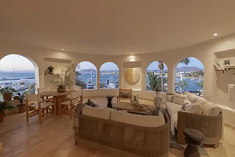 Stunning coastal views frame this elegant living space, where arched windows showcase the marina and surrounding hillsides. Picture yourself relaxing on plush seating while boats drift by just beyond your retreat.