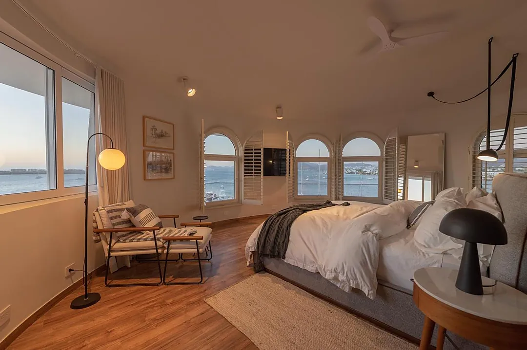 Bedroom 1 (Master) · Your serene bedroom retreat features gleaming hardwood floors, a cozy seating nook by arched windows, and breathtaking water views that greet you each morning.