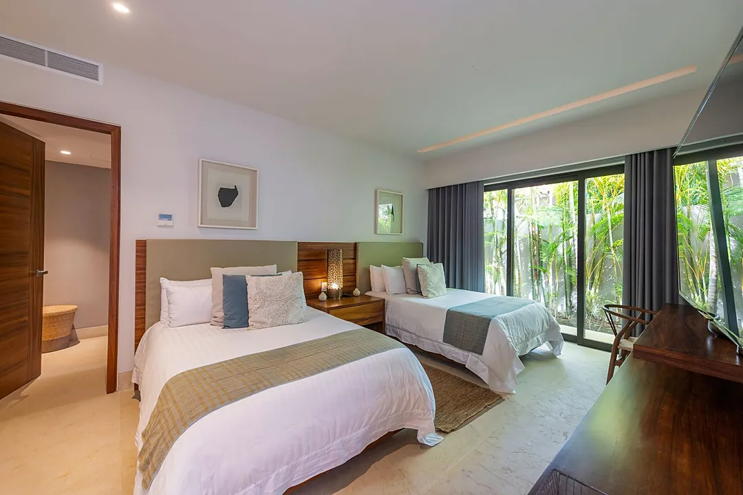 Bedroom 4 · Drift off in your serene twin bedroom, where crisp white linens and lush garden views through floor-to-ceiling windows invite deep relaxation.
