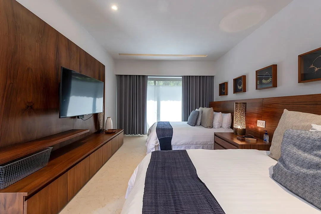Bedroom 3 · Settle into crisp white linens and modern comforts—this stylish bedroom features rich wood accents, a flat-screen TV, and soft natural light filtering through the windows.