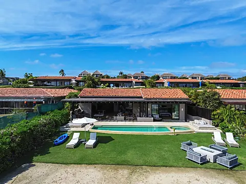This stunning villa features a private pool, lush lawn, and multiple lounging areas under clear blue skies. Tile-roofed architecture blends seamlessly with vibrant coastal surroundings.