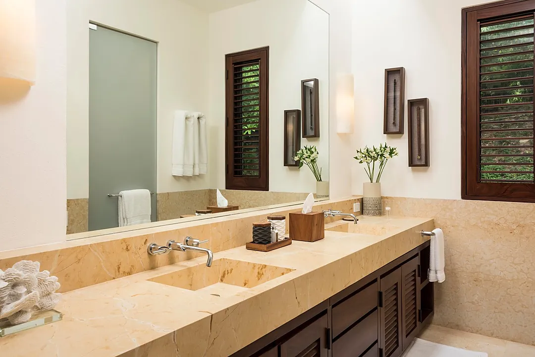 Bathroom 2 · Step into this serene bathroom where warm stone counters and tropical shutters create your private retreat. Fresh blooms and soft towels await your arrival.