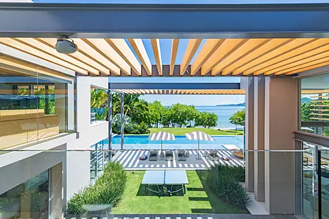 A striking pergola frames your private pool and manicured lawn, with the shimmering sea stretching beyond lush tropical gardens—an idyllic outdoor retreat for sun-soaked relaxation.