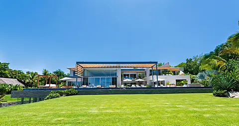A stunning contemporary estate set within a lush tropical landscape. The expansive manicured lawn and surrounding palm trees frame this architectural showpiece, promising a luxurious private retreat.