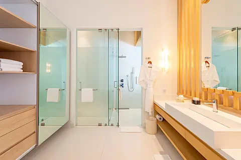 Bathroom 2 · Refresh and recharge in your bright, modern bathroom, complete with a rainfall shower, plush robe, and sleek vanity, all designed with clean lines and calming coastal tones.