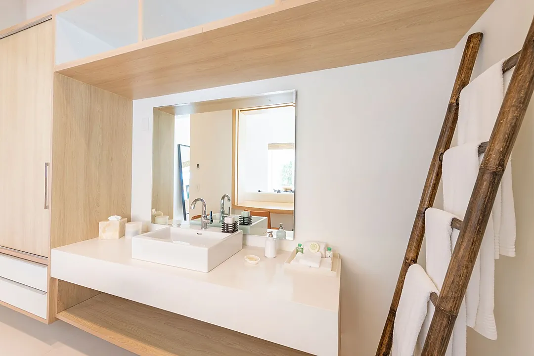 Bathroom 2 · You'll feel instantly refreshed in this bright, serene bathroom with its sleek modern sink, warm wood tones, and charming rustic ladder holding plush white towels.