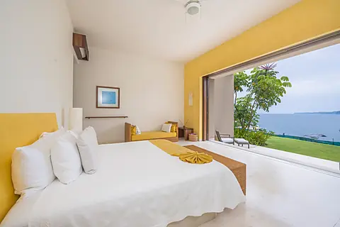 Relax in your serene living space, where floor-to-ceiling windows frame peaceful water views and lush green lawns, blending modern comfort with tropical island beauty.