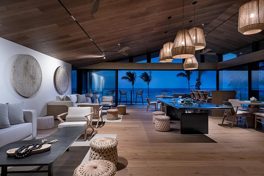 Step into your spacious open-plan living and dining area, where natural textures and warm wood tones create a serene coastal retreat. Floor-to-ceiling windows frame stunning ocean views and swaying palms just beyond your private terrace.