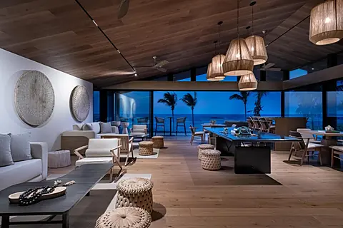 Step into your spacious open-plan living and dining area, where natural textures and warm wood tones create a serene coastal retreat. Floor-to-ceiling windows frame stunning ocean views and swaying palms just beyond your private terrace.