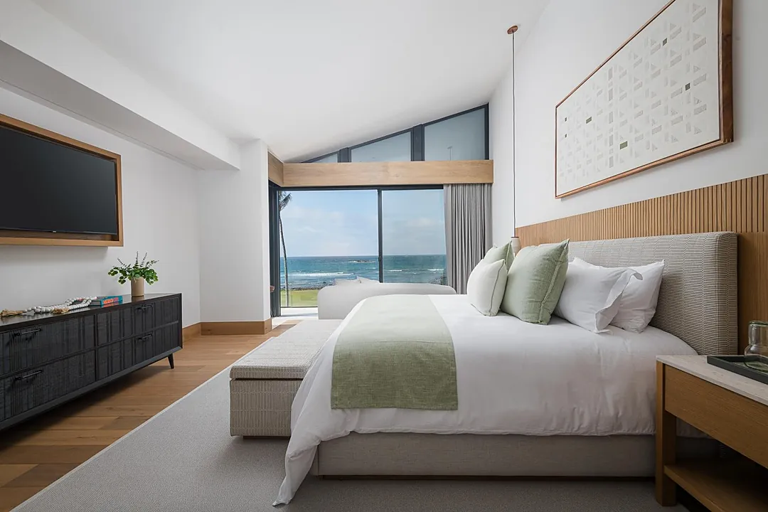 Bedroom 1 (Master) · Drift off to the gentle rhythm of ocean waves as natural light fills your serene bedroom. Wake to soothing seafront views framed by floor-to-ceiling windows, with crisp linens and modern coastal design creating your perfect retreat.