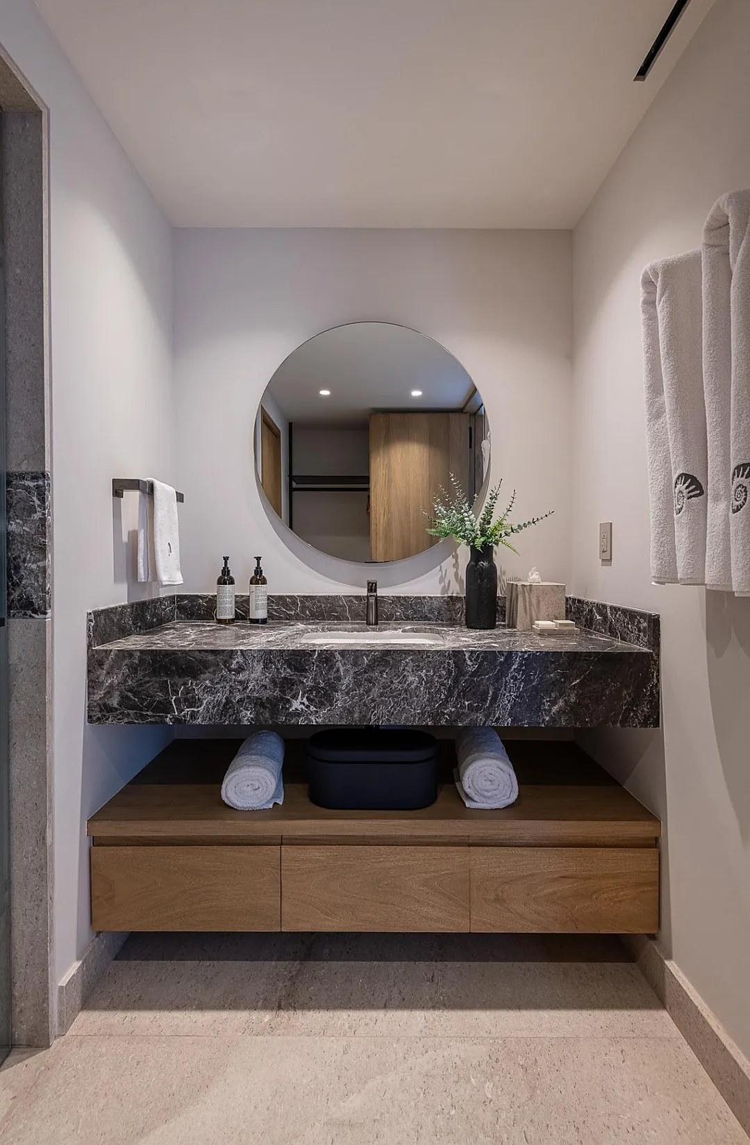 Bathroom 3 · Unwind in your private sanctuary, where sleek marble meets warm wood tones. Fresh towels await beneath a statement mirror, while thoughtful touches and greenery create a spa-like retreat.