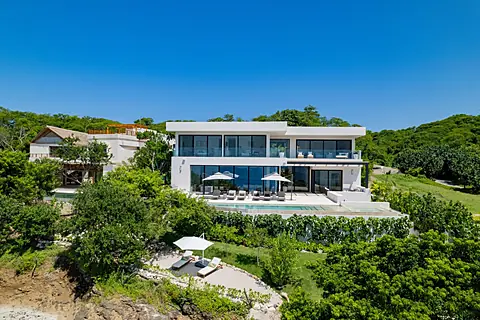 A stunning modern villa nestled into lush tropical hillside, featuring a private pool and spacious terraces surrounded by vibrant greenery and ocean breezes.