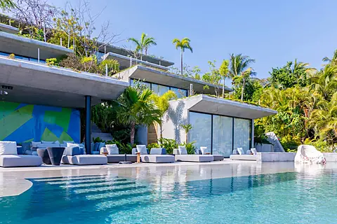A stunning modern retreat surrounded by lush tropical gardens. Relax on the pristine pool deck or unwind in the stylish lounging areas framed by swaying palms and vibrant greenery.