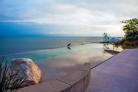 The infinity pool reflects a dramatic sky and seamlessly merges with the open water beyond. A peaceful beachfront setting where modern design meets natural beauty.