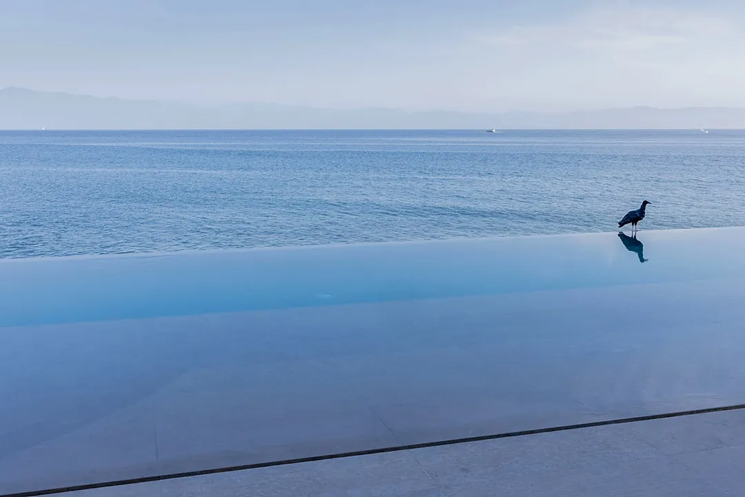 A serene infinity pool blends seamlessly with the calm ocean beyond, as distant mountains frame this peaceful coastal retreat.