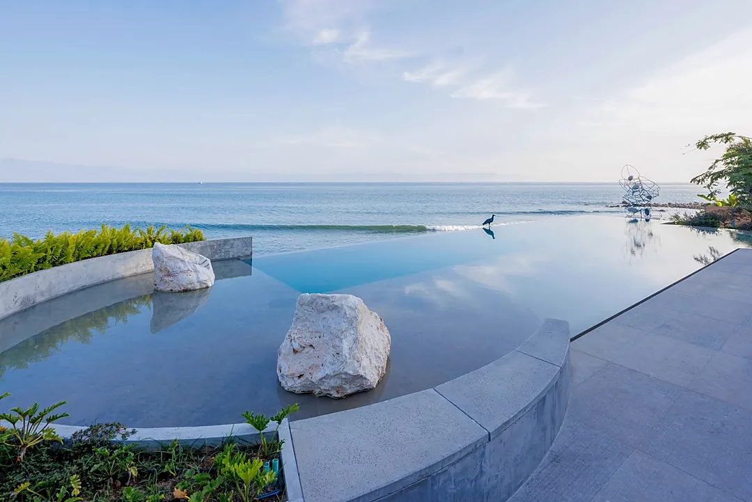 An infinity pool merges seamlessly with the ocean beyond, framed by sculptural stones and modern design—a tranquil escape where the horizon feels within reach.
