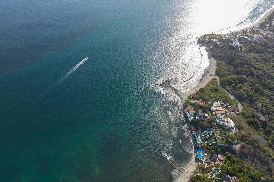 An aerial perspective captures the coastal resort area nestled along pristine beaches, where turquoise waters meet white sand and lush tropical vegetation shelters the surrounding properties.