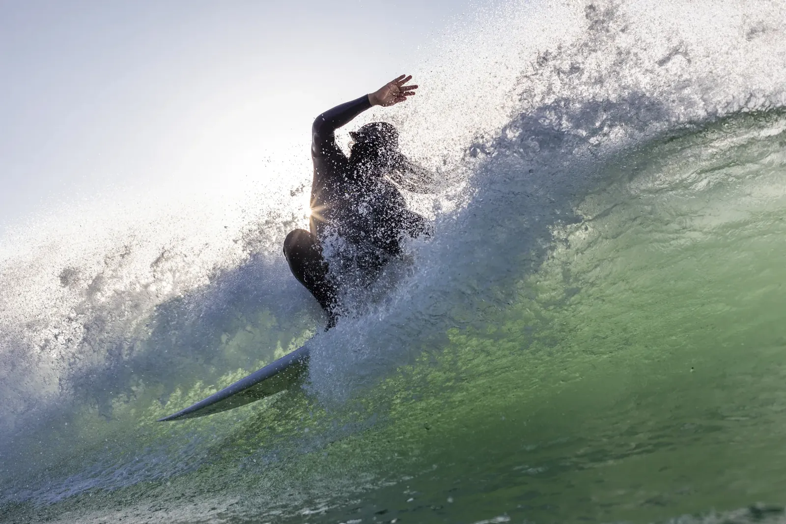 Surfer carving off the top of a backlit wave